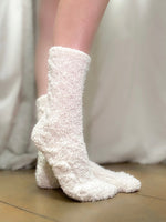 White fuzzy socks worn by a person on a neutral background