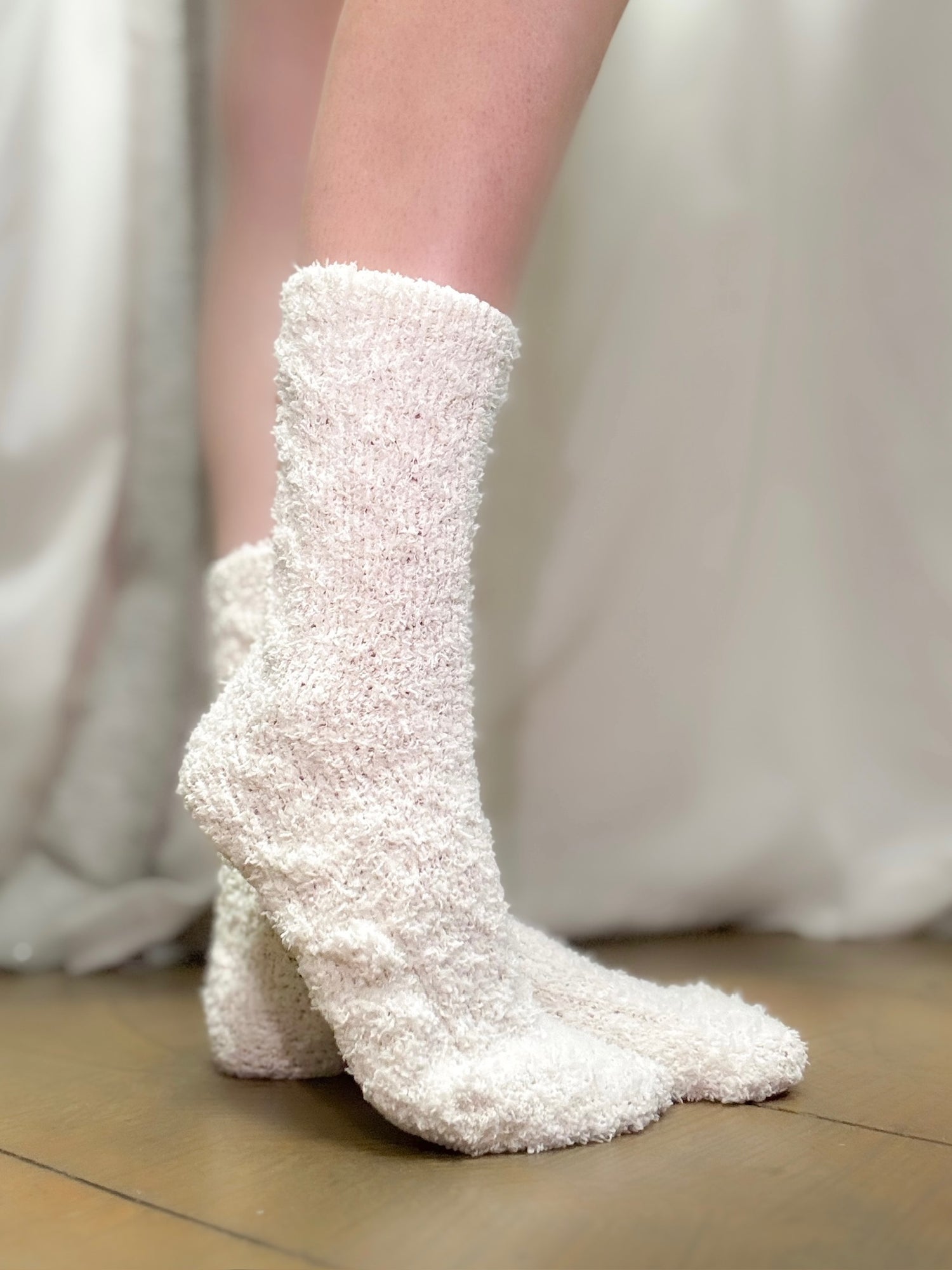 White fuzzy socks worn by a person on a neutral background