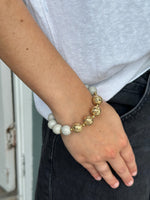 Person wearing a bracelet with gold and white beads on a neutral background
