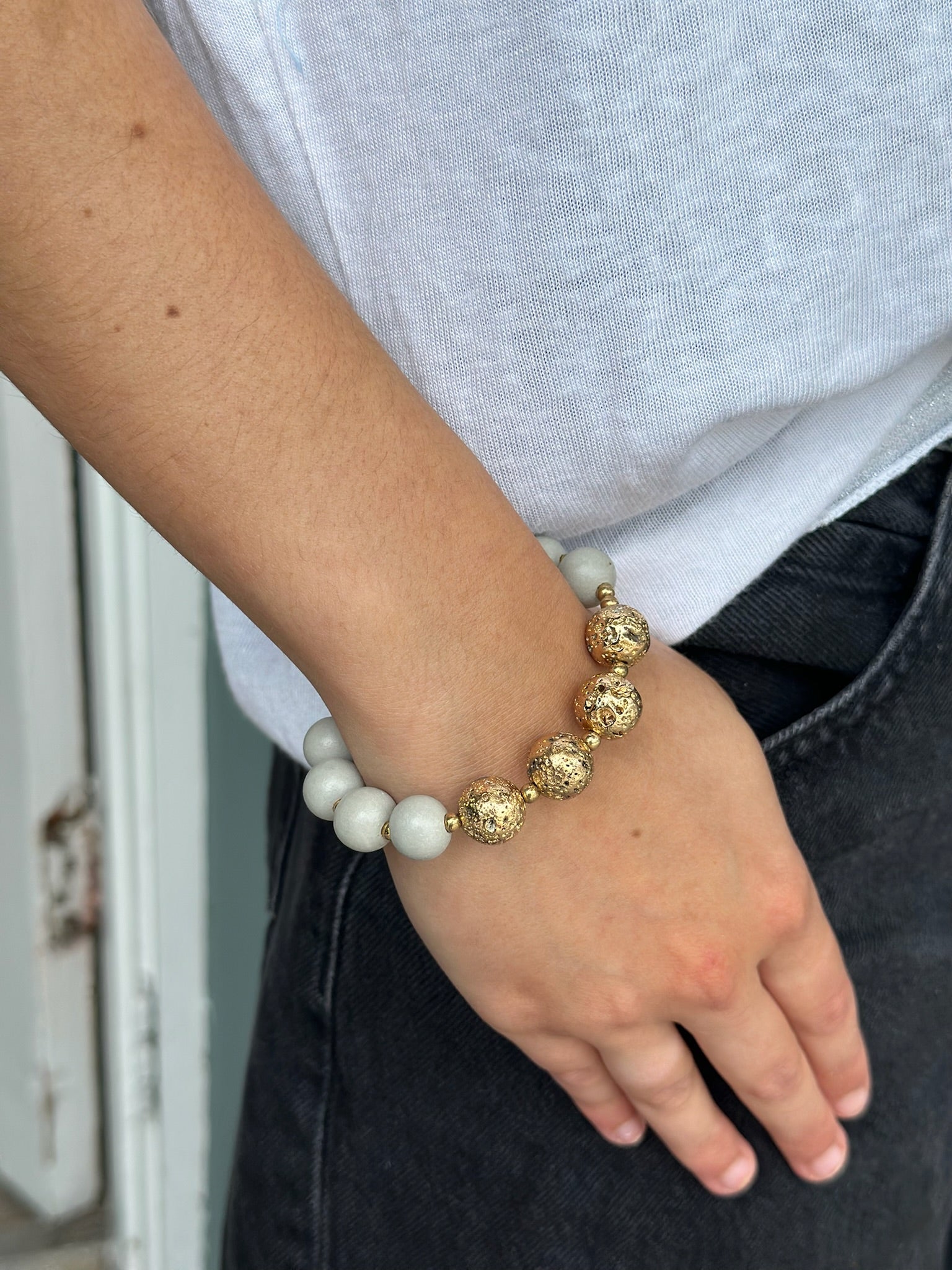 Person wearing a bracelet with gold and white beads on a neutral background