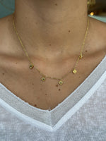 Gold necklace with small pendants on a person wearing a white shirt.