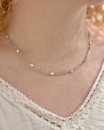 Silver necklace with small beads on a person wearing a lace top.