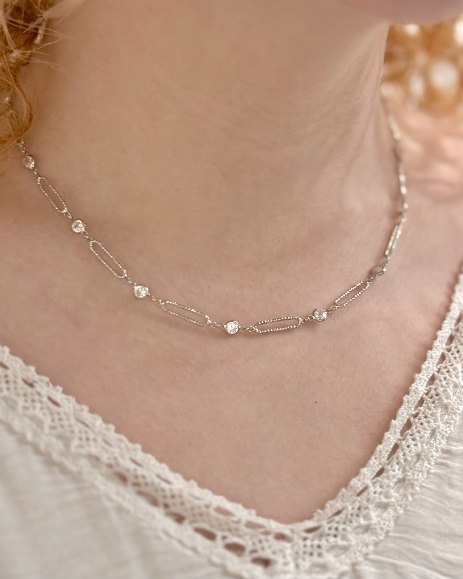Silver necklace with small beads on a person wearing a lace top.