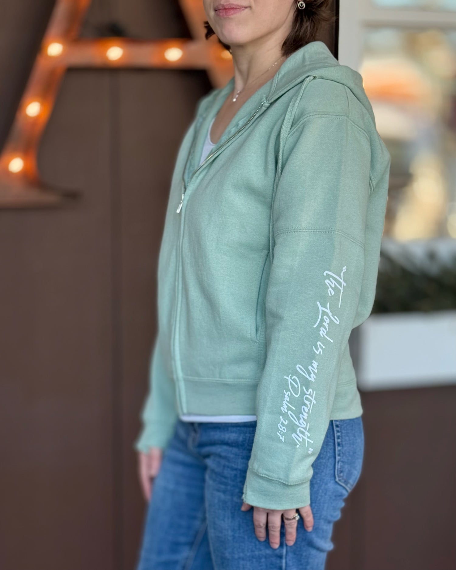Woman wearing The Lord is my strength script on sleeve of a hoodie standing outside ardor boutique 
