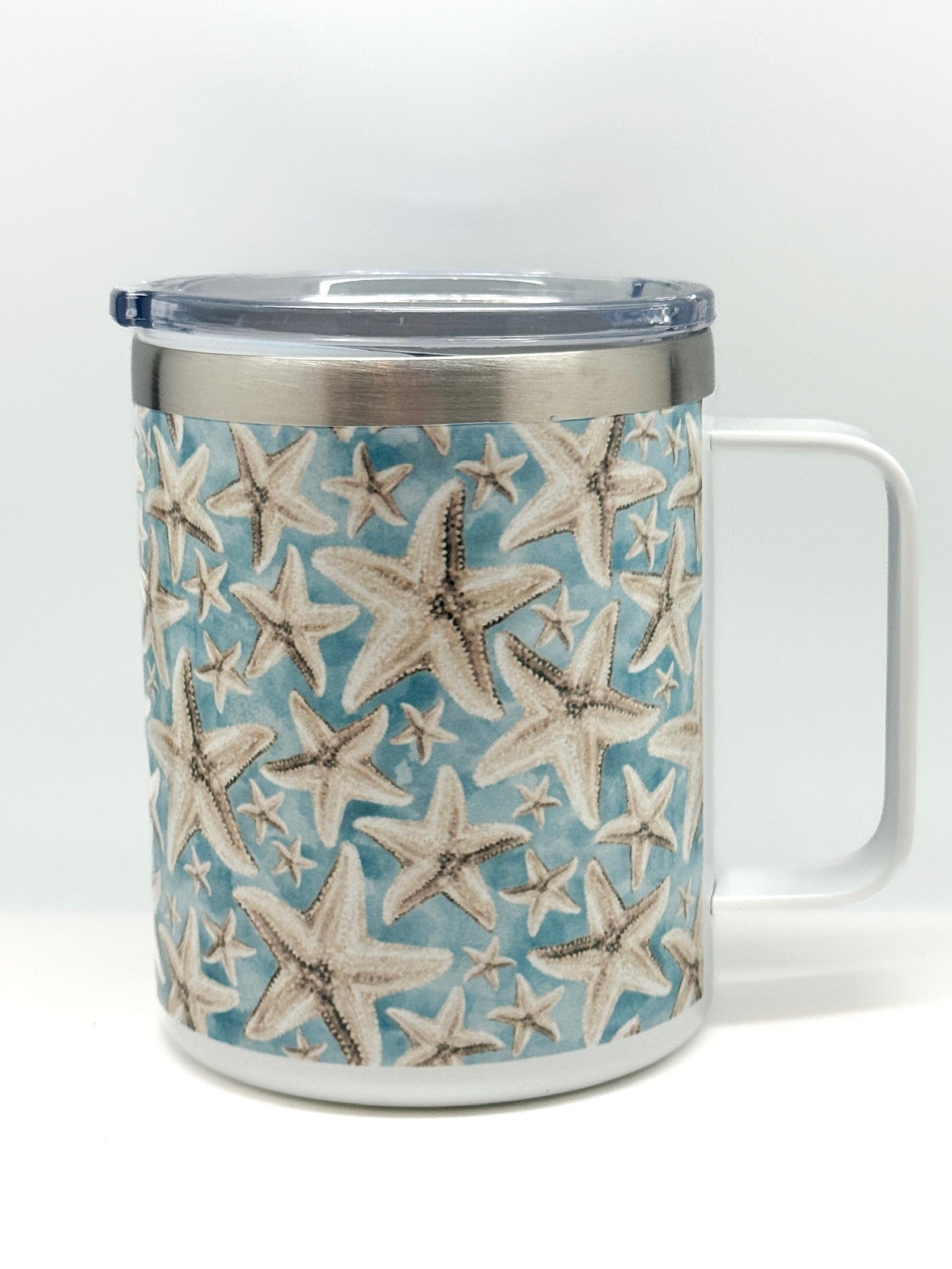 Travel mug with handle and clear lid, featuring sandy starfish pattern on a blue background