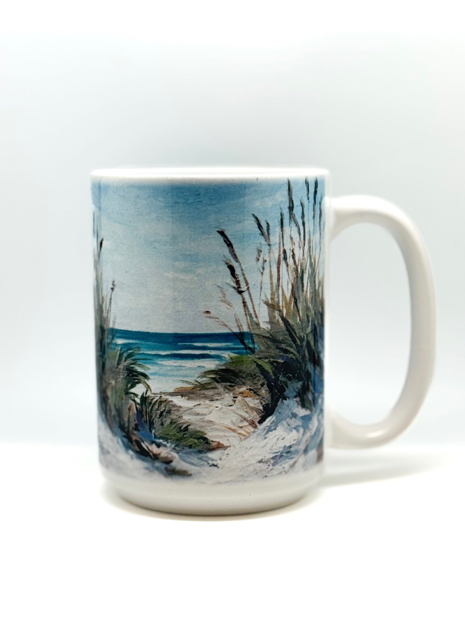 Ceramic mug featuring a painted seascape design with sandy dunes, tall grasses, and ocean waves in the background.
