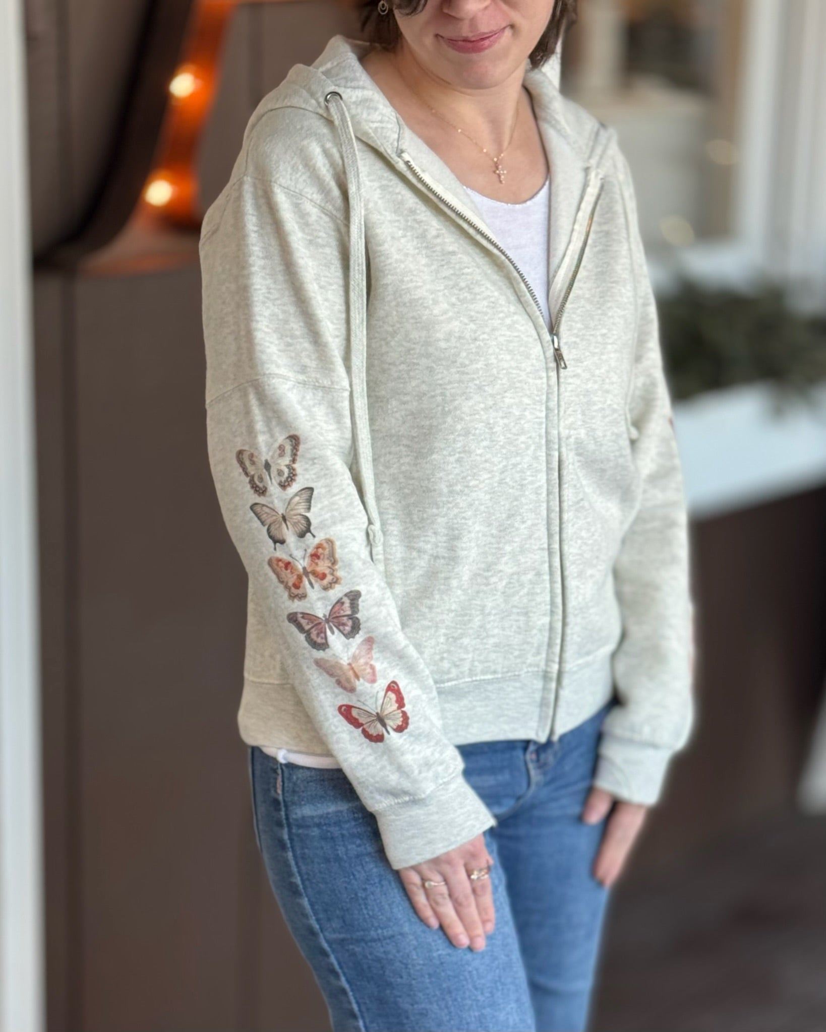 woman wearing an oatmeal hoodie with pink red butterfly design on sleeve