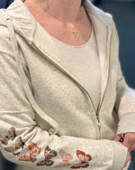 Person wearing a light gray hoodie with butterfly designs on the sleeves, standing against a blue background.