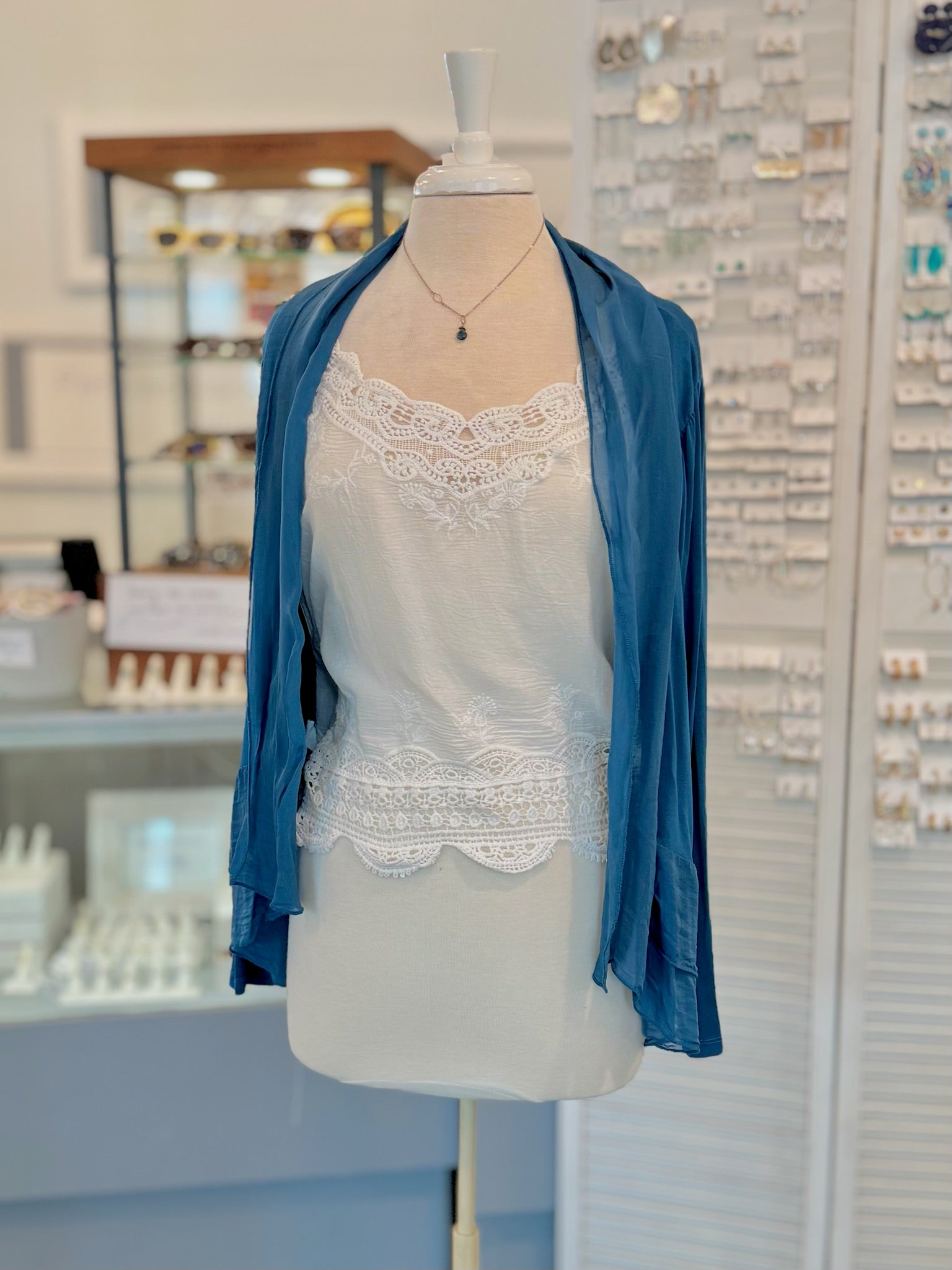 Mannequin wearing a blue cardigan over a white lace top in a store setting