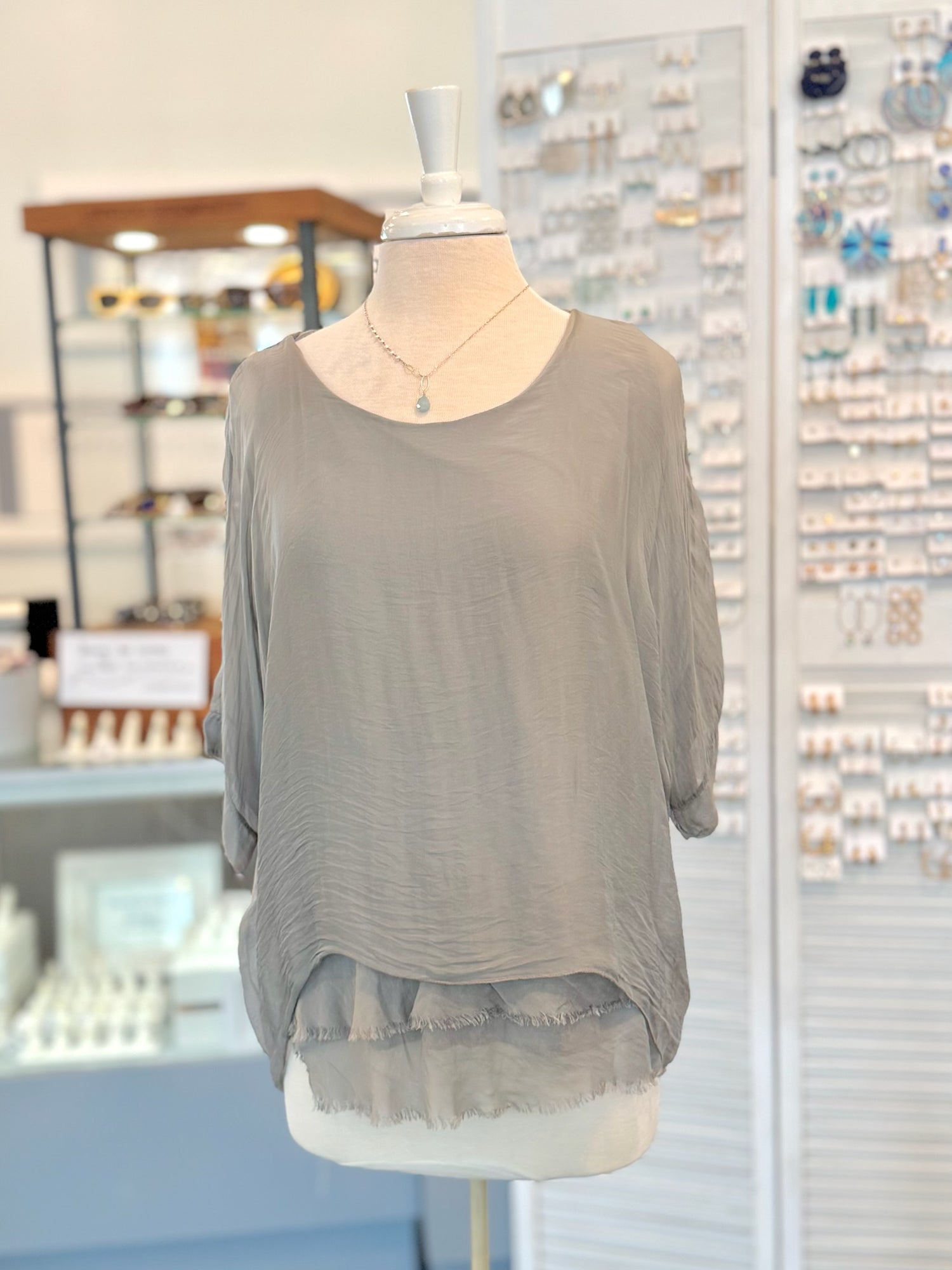 Gray blouse on a mannequin in a store setting with jewelry displays.