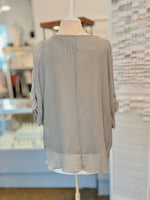 Light gray blouse on a mannequin against a blurred indoor background