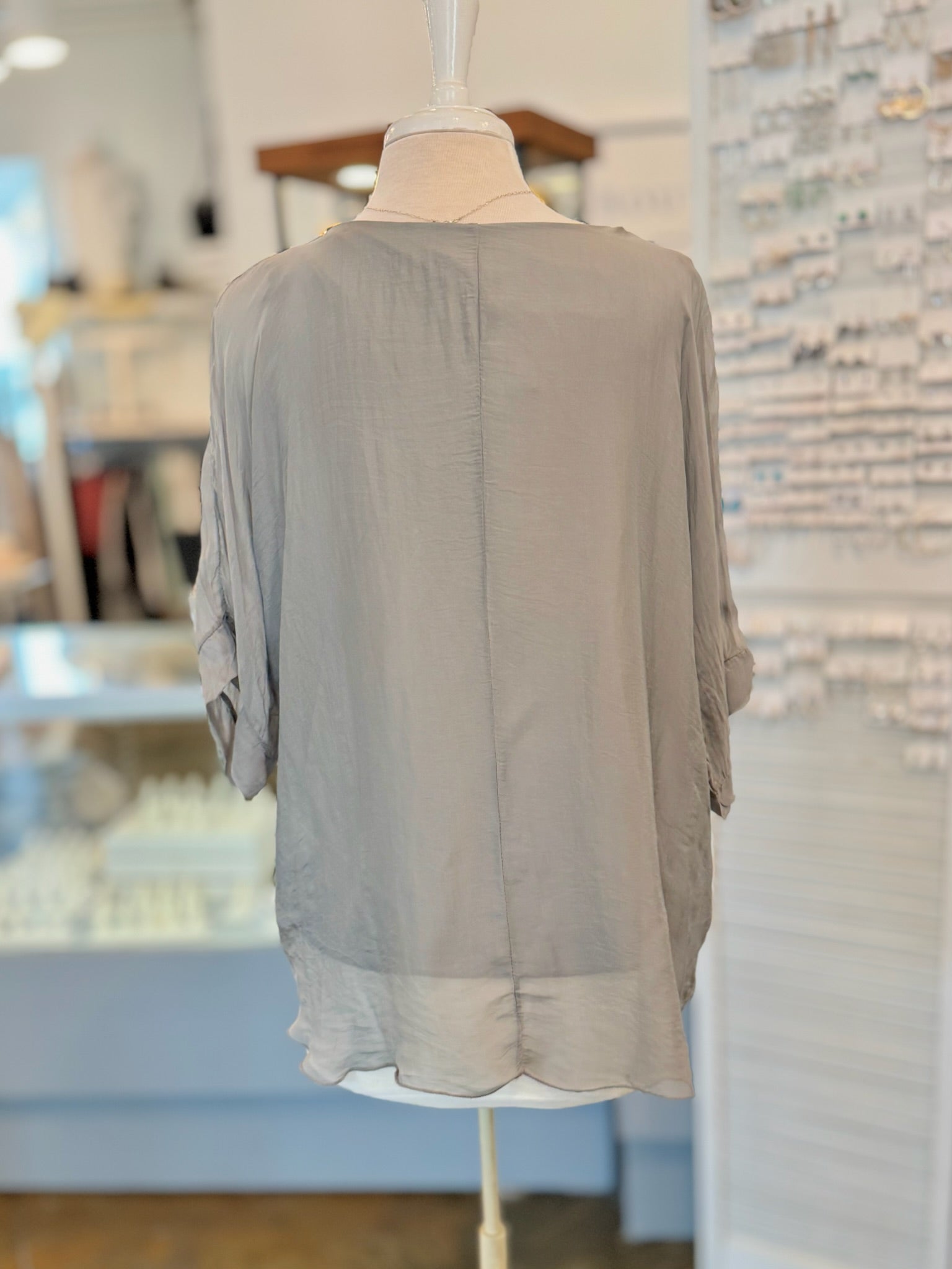 Light gray blouse on a mannequin against a blurred indoor background