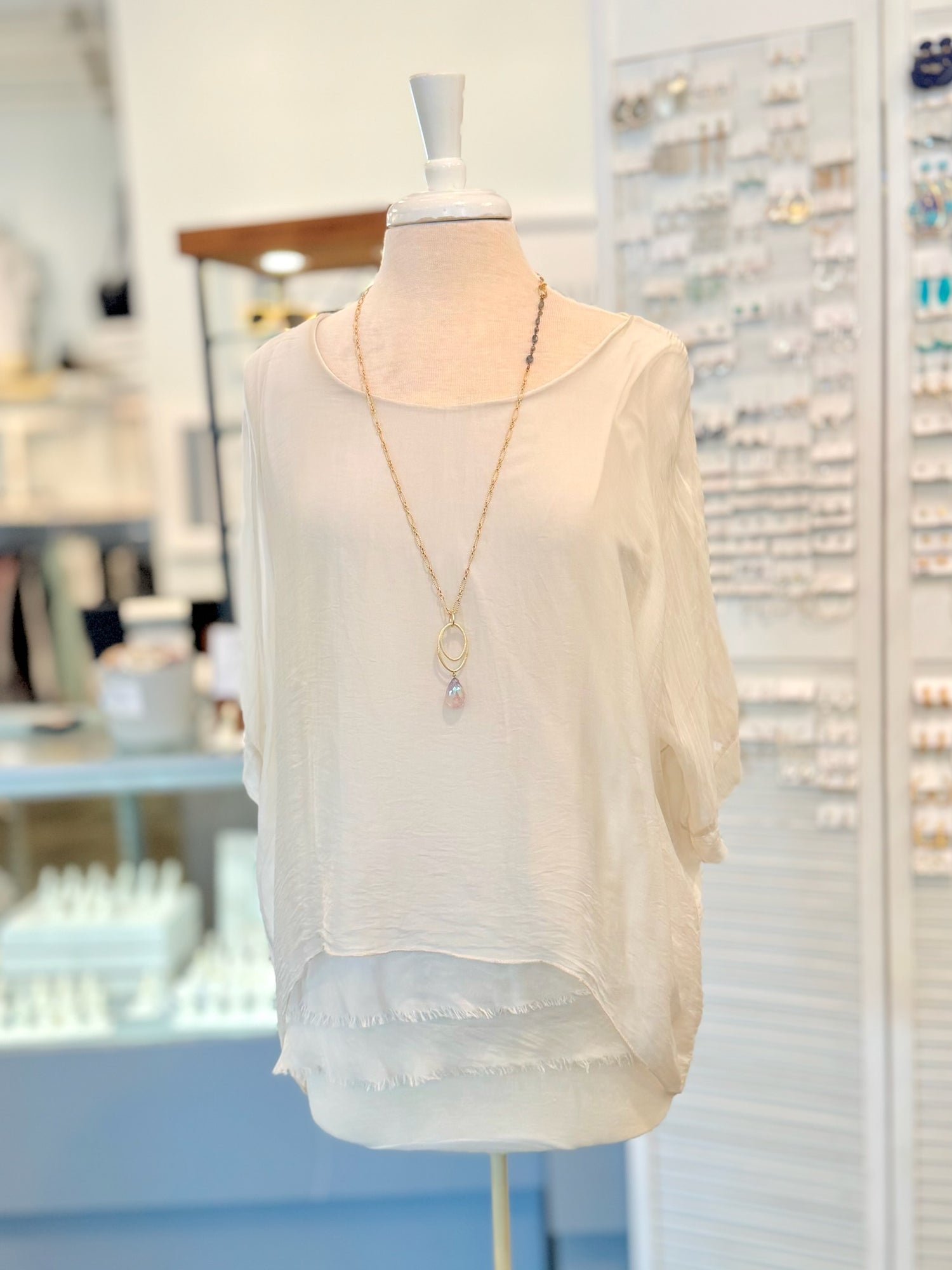 Mannequin wearing a light-colored blouse with a necklace in a store setting