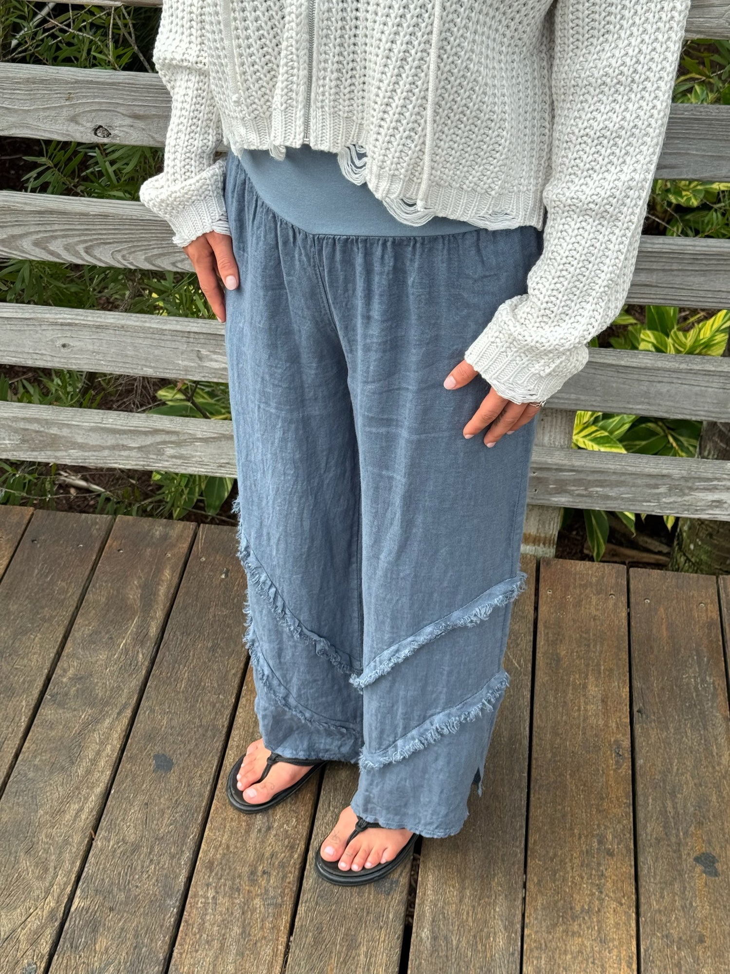 Casual blue-gray linen pants with diagonal frayed trim and wide-leg design, styled with a knit sweater.