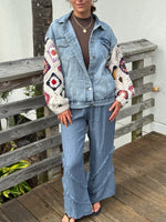 Model wearing A light-wash denim jacket with colorful crocheted sunset sleeves.
