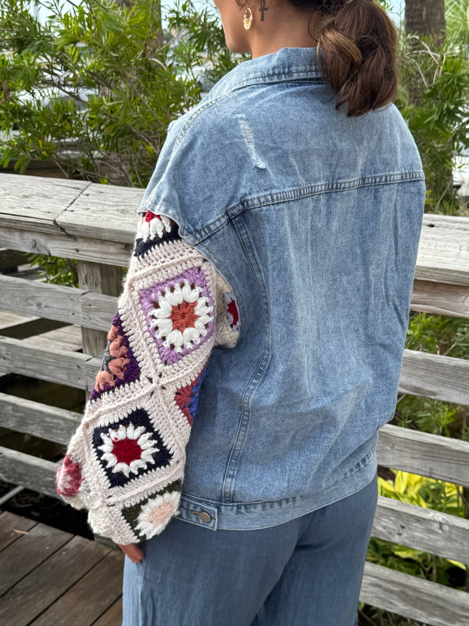 Model wearing A light-wash denim jacket with colorful crocheted sunset sleeves.