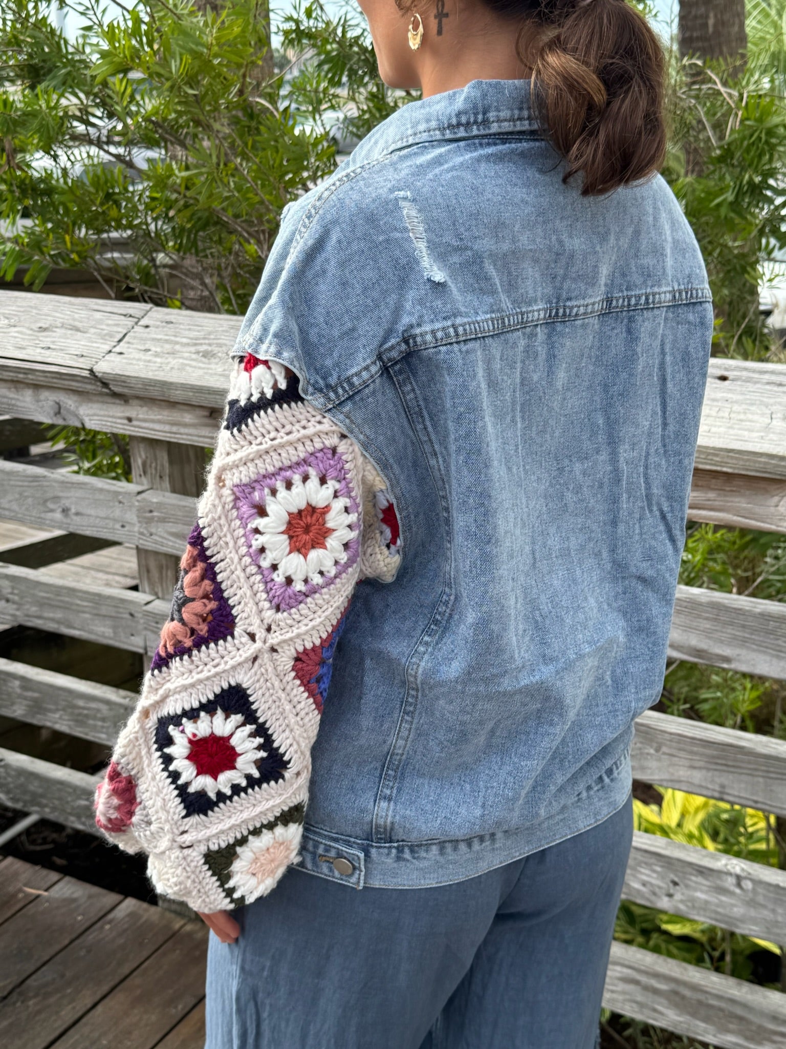 Model wearing A light-wash denim jacket with colorful crocheted sunset sleeves.