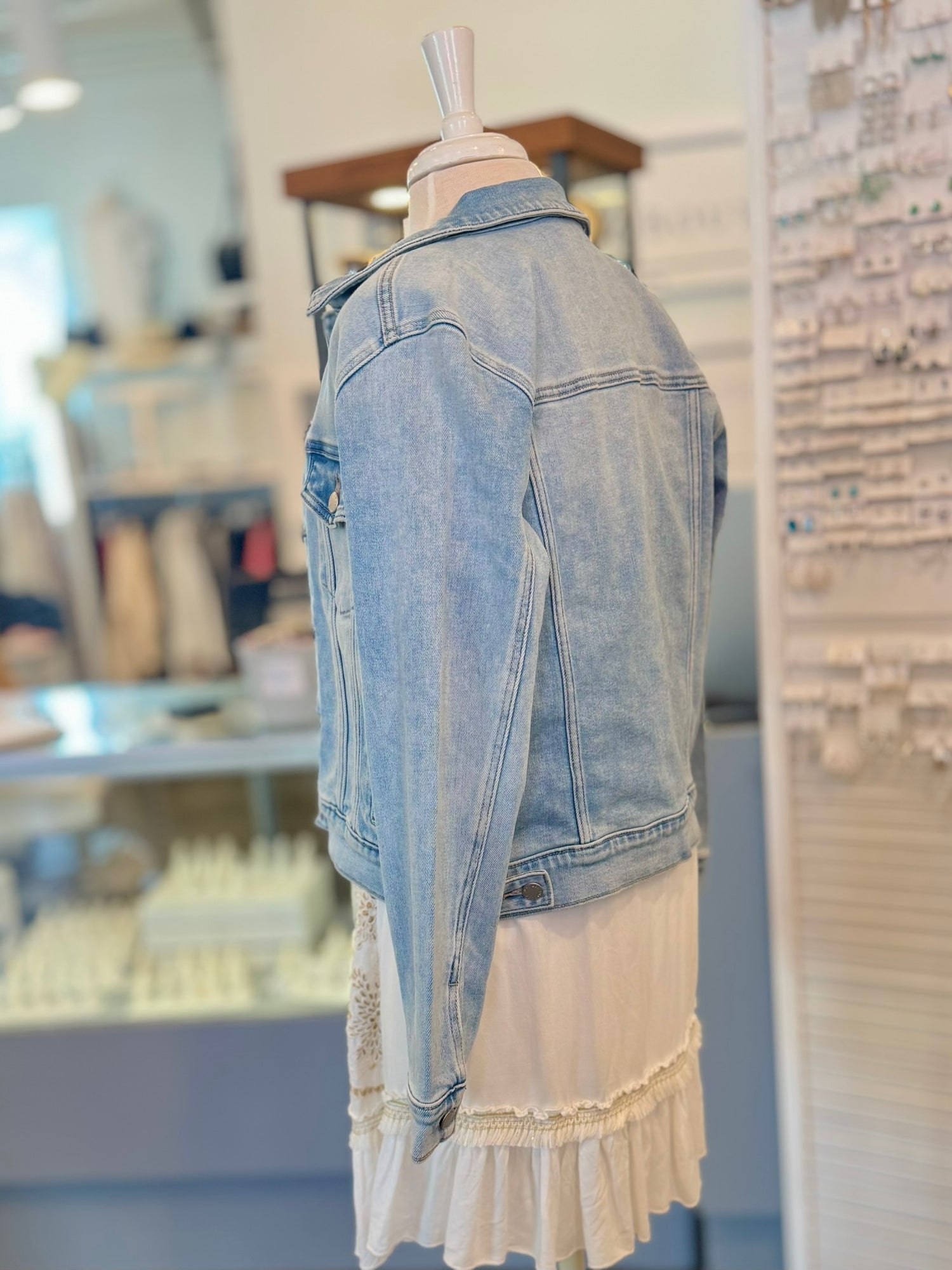 Side view of mannequin wearing a light blue denim jacket over a white dress in a store setting.