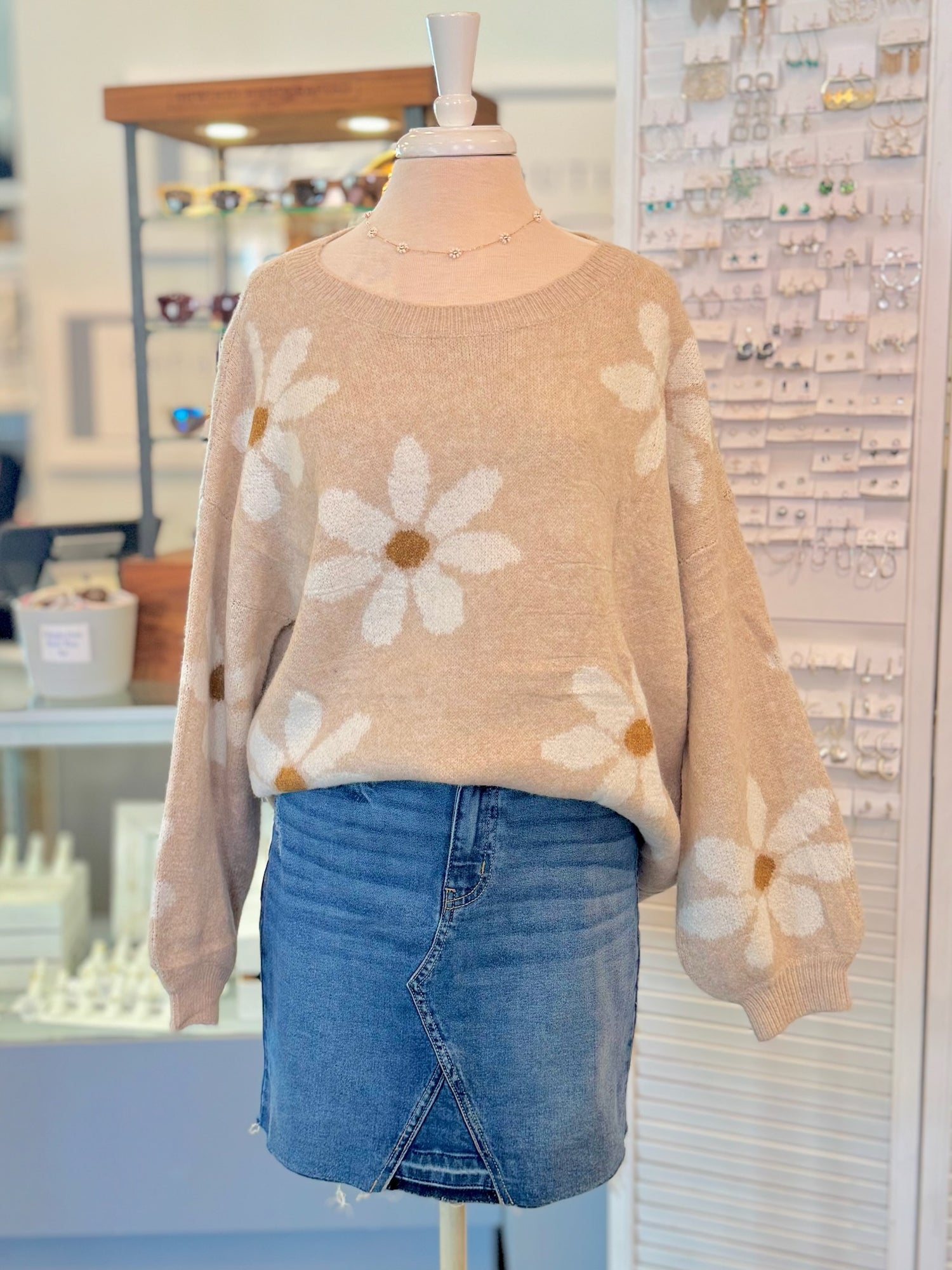 Mannequin wearing a beige sweater with floral patterns and blue denim skirt in an indoor setting.