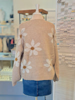 Back view of mannequin wearing a beige sweater with floral patterns and blue denim skirt in an indoor setting.