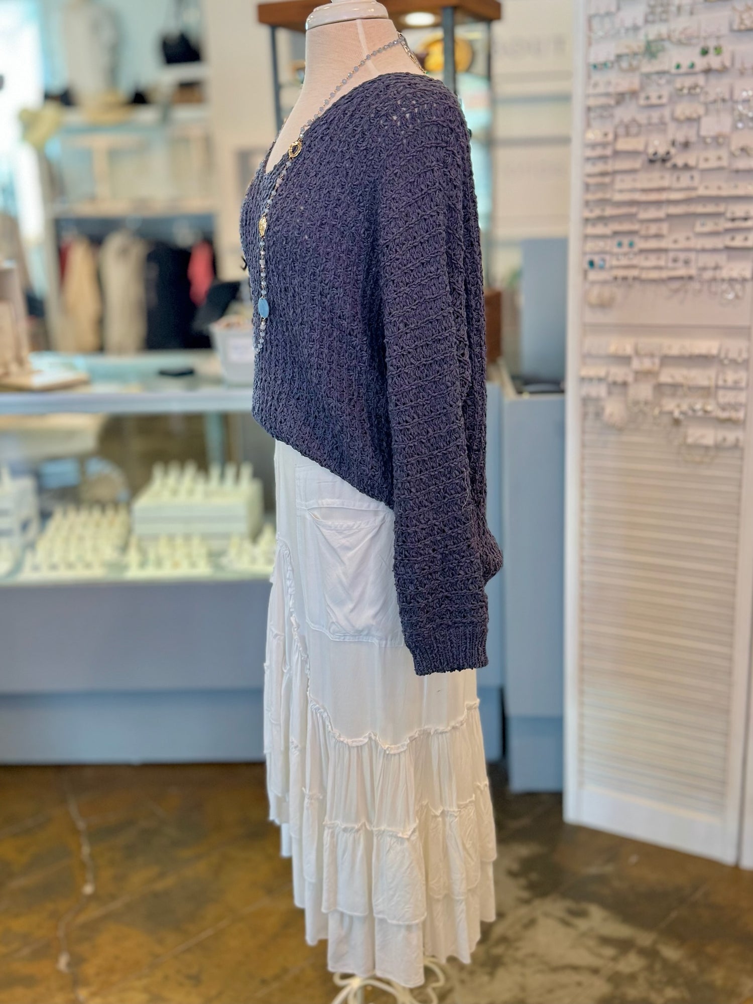 Mannequin wearing a blue knitted cardigan over a white dress in a store setting.