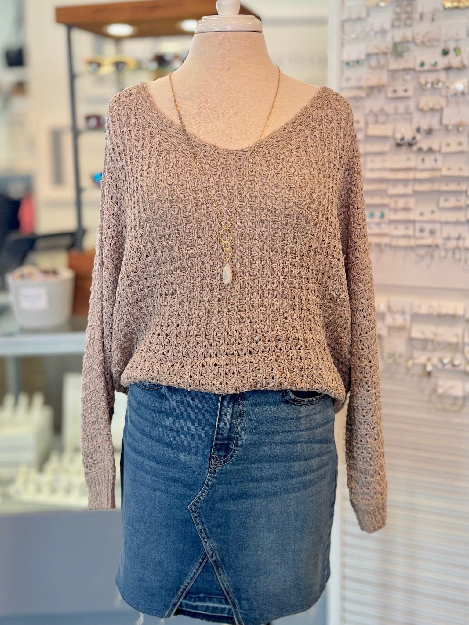 Mannequin wearing a brown knitted sweater tucked in and blue jean skirt in a store setting