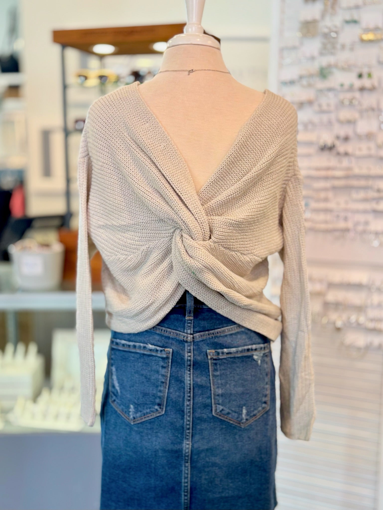 Mannequin wearing a beige sweater with a knot detail and blue jean skirt in a store setting