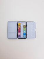 Set of watercolor paints in a portable case on a light gray background
