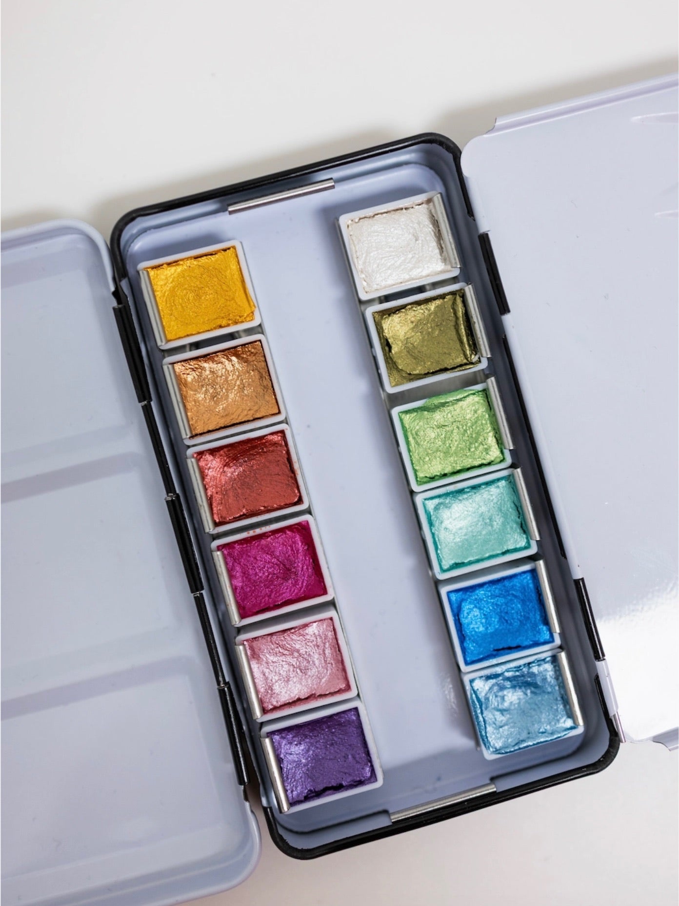 Open watercolor palette with various colors on a white background