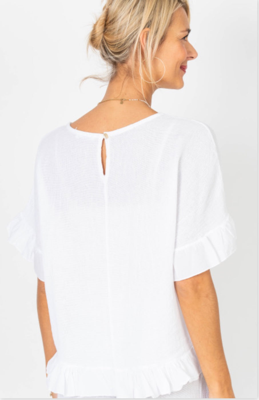 Woman wearing a white blouse with a cut-out back design on a plain background