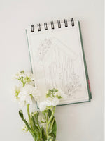 Notebook with architectural drawing and white flowers on a light surface