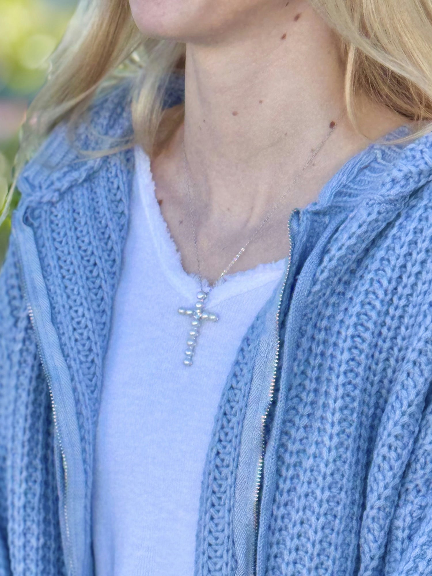 Person wearing a light blue zip-up hoodie and a white shirt with a cross necklace.