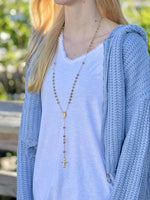 Long gold rosary necklace worn layered over a soft knit top