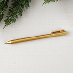 Gold pen with white "joy" text on a light gray fabric background with greenery