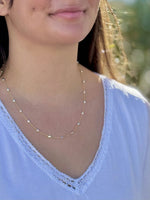 Close-up of a person wearing a delicate gold necklace with a blurred natural background
