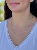 Close-up of a person wearing a delicate necklace with a blurred natural background