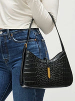 Person wearing a black crocodile-patterned handbag with a white background
