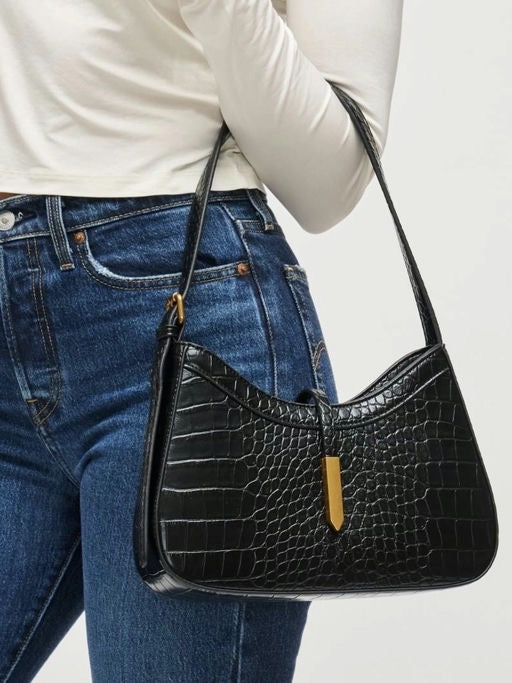 Person wearing a black crocodile-patterned handbag with a white background