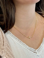 Gold necklace with a small cross pendant worn by a person.
