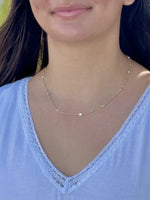 Model wearing a gold plated sterling silver station necklace with small round accents, styled with a white lace-trim top