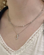 Close-up of a person wearing a delicate necklace with a cross pendant.