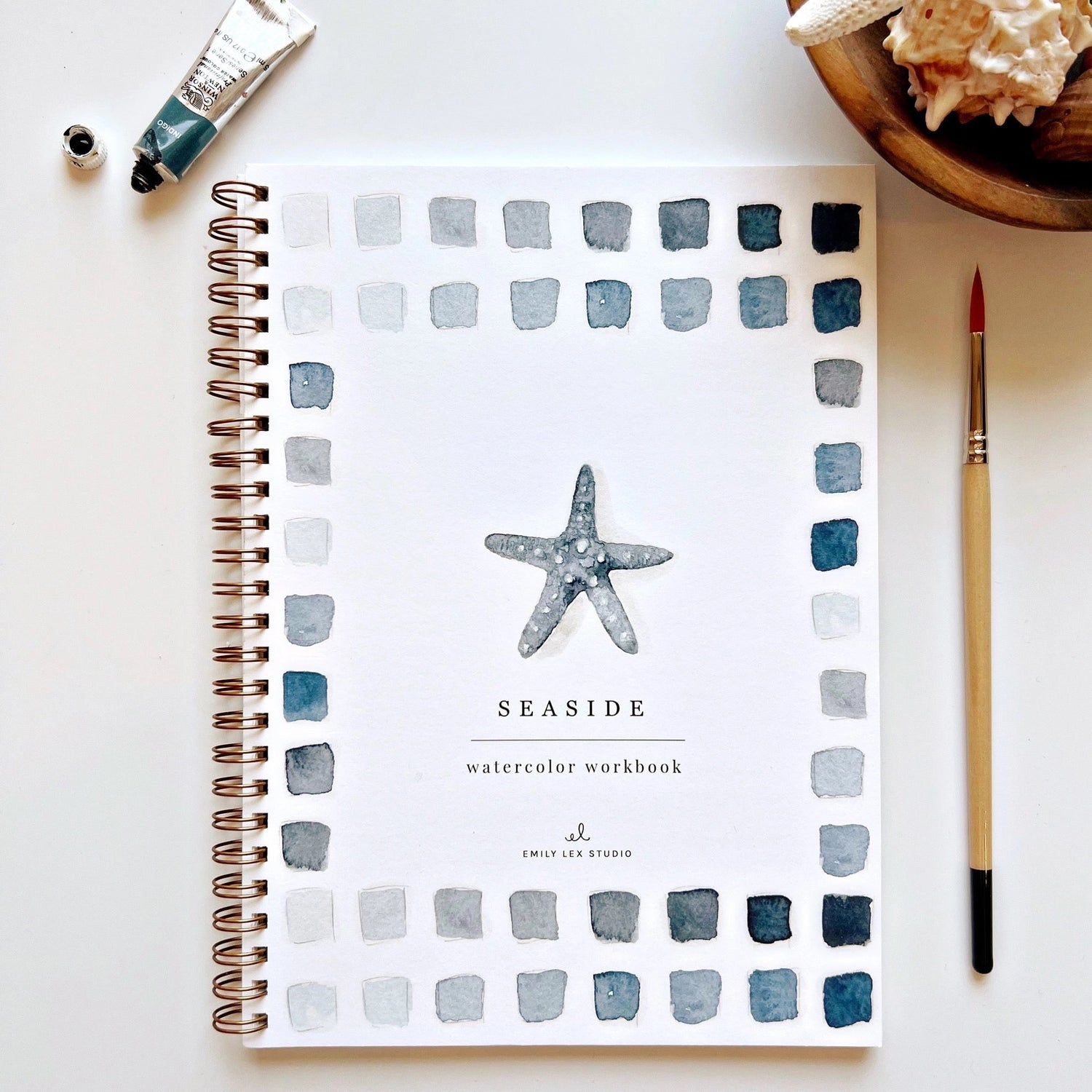 Seaside watercolor workbook with starfish design on a white surface with art supplies.