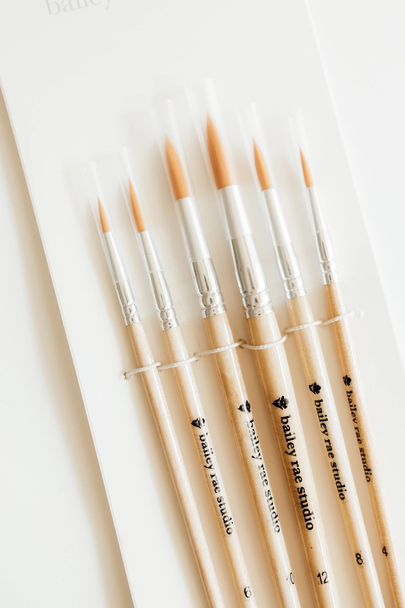 “Set of round watercolor paint brushes with wooden handles and protective plastic tips on a white background.”