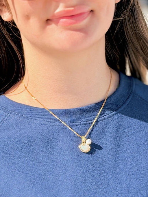 Person wearing a gold necklace with a seashell pendant on a blue shirt