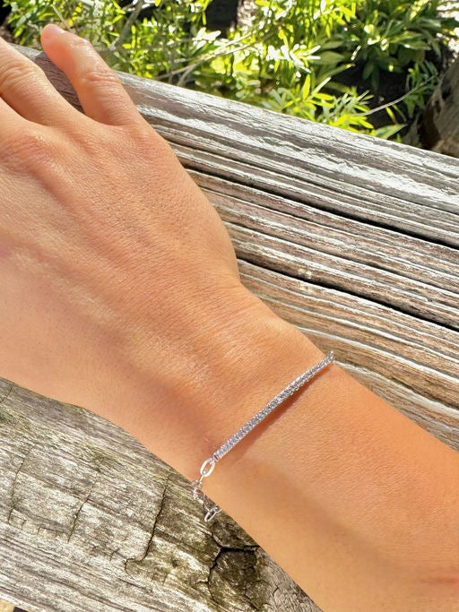 Hand wearing a silver bracelet on a wooden surface with greenery in the background