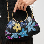Handbag with floral embroidery held by a person against a neutral background