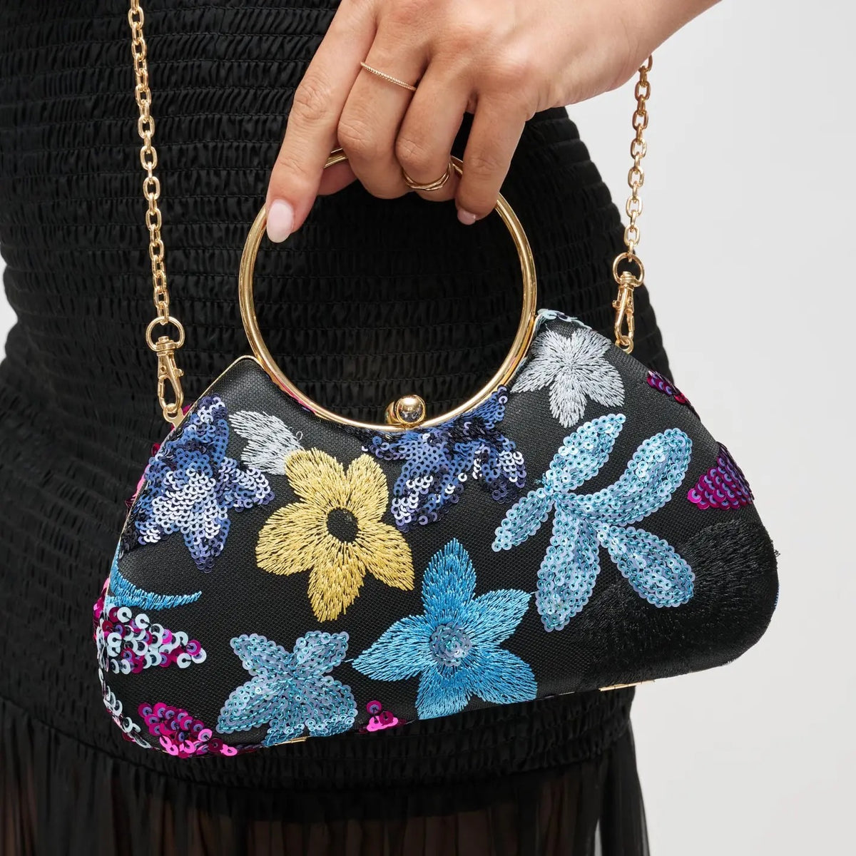 Handbag with floral embroidery held by a person against a neutral background