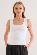 Model wearing a white square-neck sleeveless fitted tank top with wide straps, styled with black pants at Ardor Boutique.
