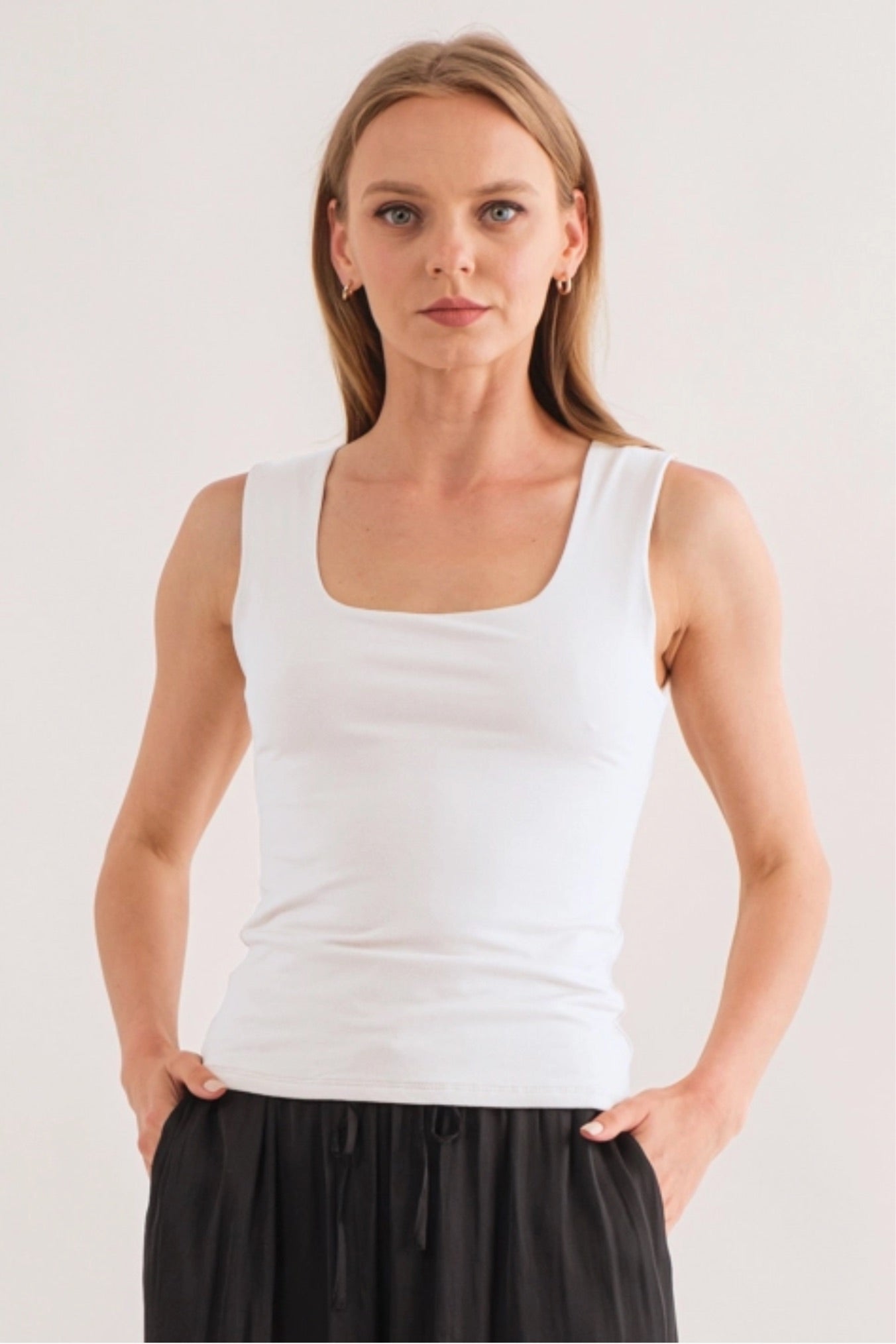 Model wearing a white square-neck sleeveless fitted tank top with wide straps, styled with black pants at Ardor Boutique.
