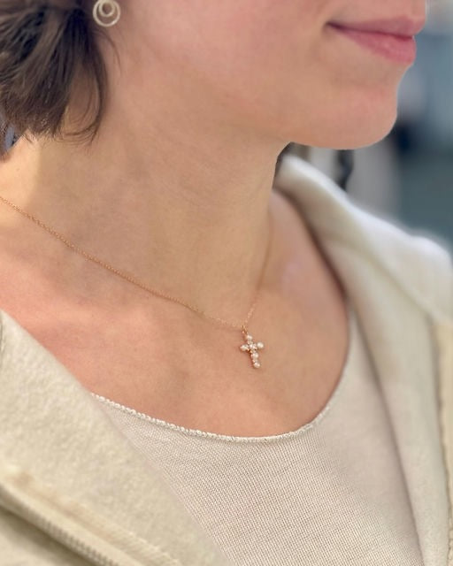 Close-up of a person wearing a rose gold necklace with a cross pendant.